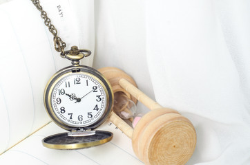 Vintage pocket watch with hourglass on white fabric background