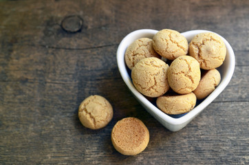 Italian Christmas cookies amaretti in a white heart shaped bowl.Tasty Italian amaretti biscuits on old wooden table.Amarettini cookies.Selective focus.