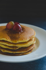 Pancakes with fresh fruit and honey on black stone background