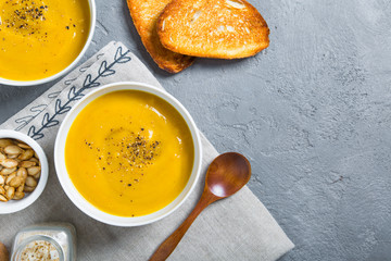 Roasted pumpkin and carrot soup with black pepper and pumpkin seeds on grey concrete background....