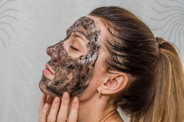 Young charming girl makes a black charcoal mask on her face
