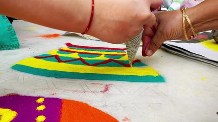 Indian women working on multicolored rangoli design on a marble floor. These designs are traditionally made during festivals like Diwali, Holi and various hindu pujas. This is made using fine colored