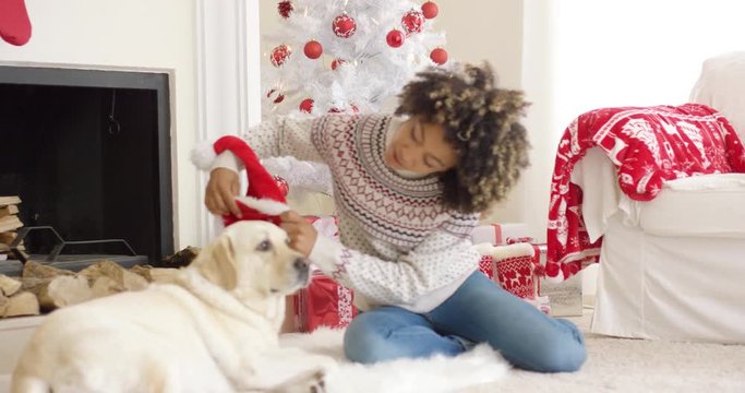 Happy smiling young woman relaxing with her dog at Christmas as they sit on a rug on the floor at the floor of the decorated red and white tree.