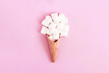 Creative minimal still life on pastel pink colored background. Waffle cone with marshmallow sweets. Copy space for text