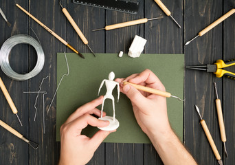 Craftsman hands working on human sculpture, sculpturing from polymer clay against working table...