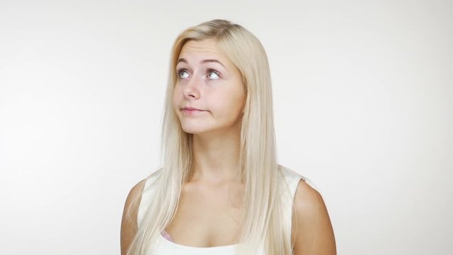 slomo frustrated thoughtful girl with long blond hair expressing uncertainty looking from side to side doubting over white background. Concept of emotions