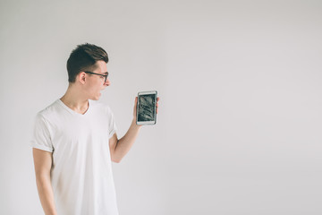 Nerd is wearing glasses. Student presenting a broken black tablet behind glass. upset man holds a...