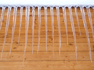 Icicles on the background of the wooden wall of the house