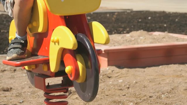 Unknown little boy in snickers ride swing in the form of horse in the courtyard of new micro district in the city outdoors