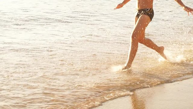 Happy Child is running on the beach at Sunset, raises splashes. Slow Motion