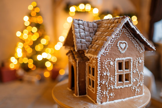 Gingerbread House Over Defocused Lights Of Chrismtas Decorated Fir Tree