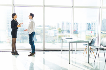 Side view of young businessman and businesswoman discussing by office window in office