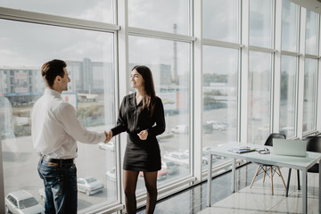 Fototapeta premium Businessman and businesswoman shaking hands together while standing in front of office building windows overlooking the city