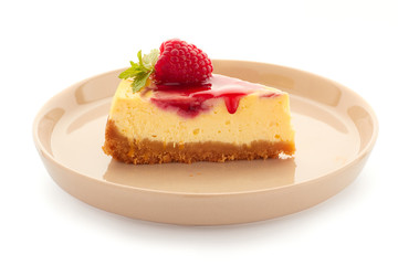 Piece of homemade cheesecake, decorated with raspberries and mint on plate over white