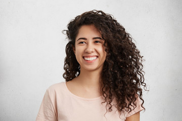 Beautiful female with curly bushy hair, mixed nationality, dressed casually, smiles broadly, shows...