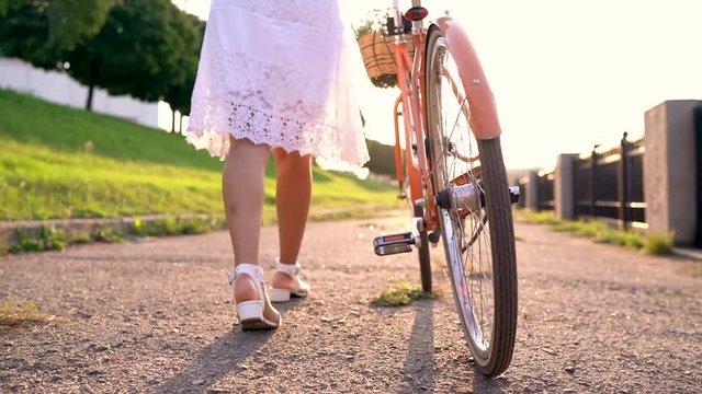 Young beautiful woman walking with a bicycle at sunset. Slow motion