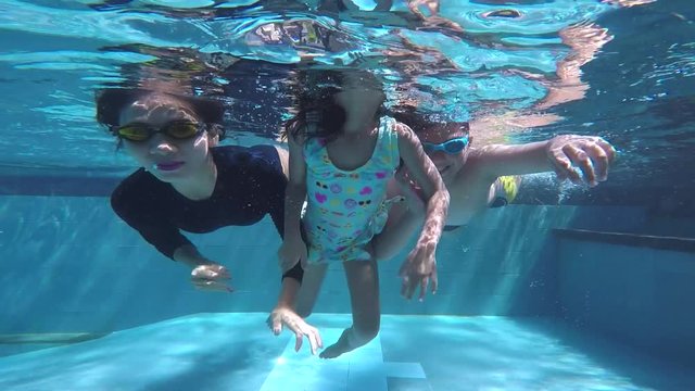 Two happy children and their mother diving together while waving hands in a pool with blue water