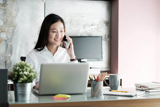 Young asian businesswoman talking smart phone while working at her office desk background, business people and communication concept, office lifestyle