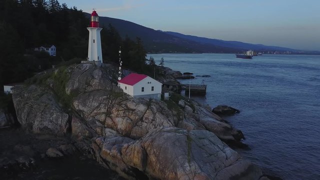 Aerial 4k footage of a lighthouse on a rocky shore during a vibrant summer sunset. Taken in Lighthouse Park, Horseshoe Bay, West Vancouver, British Columbia, Canada