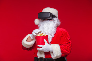 Santa Claus wearing virtual reality goggles and a red bucket with popcorn, on a red background. Christmas
