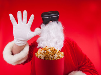 Santa Claus wearing virtual reality goggles and a red bucket with popcorn, on a red background. Christmas