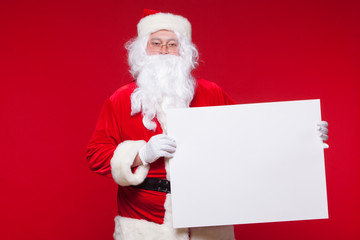 Naklejka premium Santa Claus pointing in blank advertisement banner isolated on red background with copy space