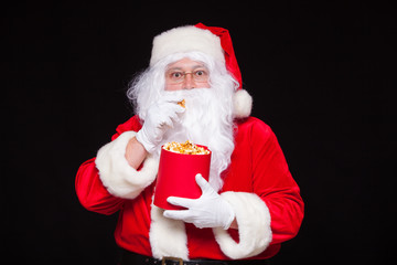 Christmas. Photo of Santa Claus gloved hand With a red bucket with popcorn, on a black background