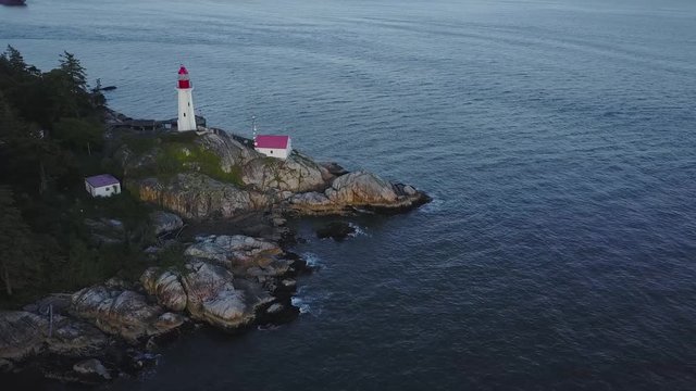 Aerial 4k footage of a lighthouse on a rocky shore during a vibrant summer sunset. Taken in Lighthouse Park, Horseshoe Bay, West Vancouver, British Columbia, Canada