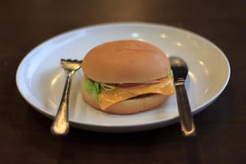The burger is placed on a white plate select focus, Burger with white plate on table Blured or blur soft focus, Cheeseburger lunch low light Blured or blur soft focus