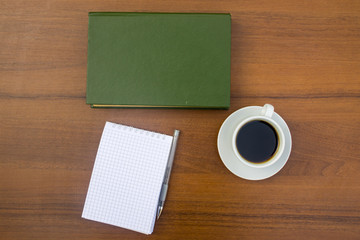 Cup of coffee, book, notepad and pen on wooden desk