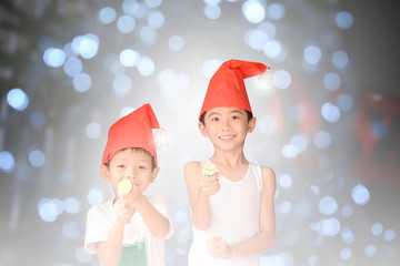 2 young asian boys wearing hand made santa claus hat playing with christmas poppers  on bokeh night light background
