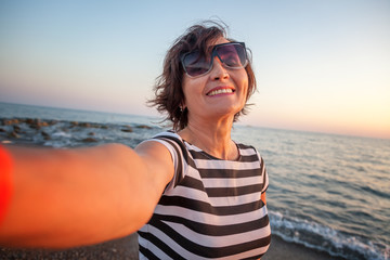 stylish attractive mature woman 50-60 makes selfie on mobile phone on the seashore, travel and...