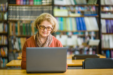 Senior woman using laptop in library. Space for text
