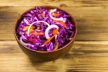 Red cabbage salad in ceramic bowl on wooden table