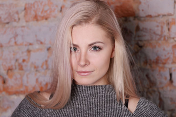 Naklejka premium portrait of beautiful blonde woman in striped blouse posing near brick wall, closeup
