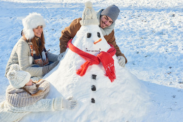 Eltern und Kind bauen einen Schneemann