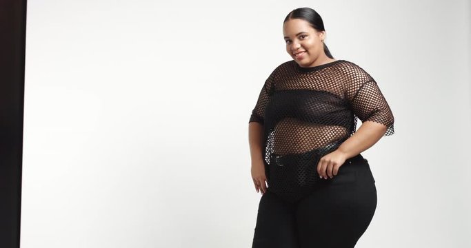 Attractive young black plus size model wearing a black fishnet top and black tight pants on white background. beauty plus size curvy model