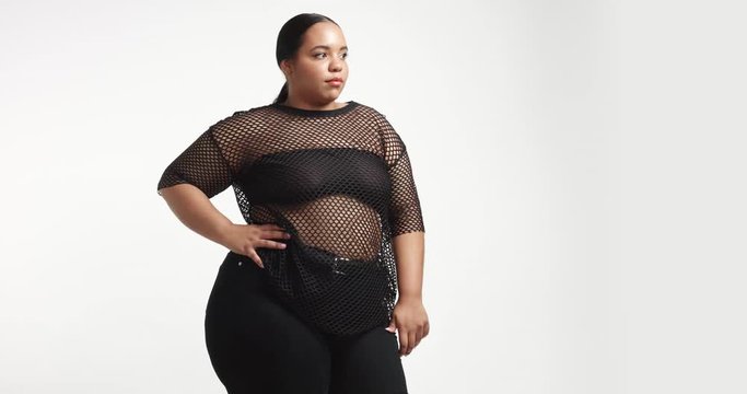 Attractive young black plus size model wearing a black fishnet top and black tight pants on white background. beauty plus size curvy model