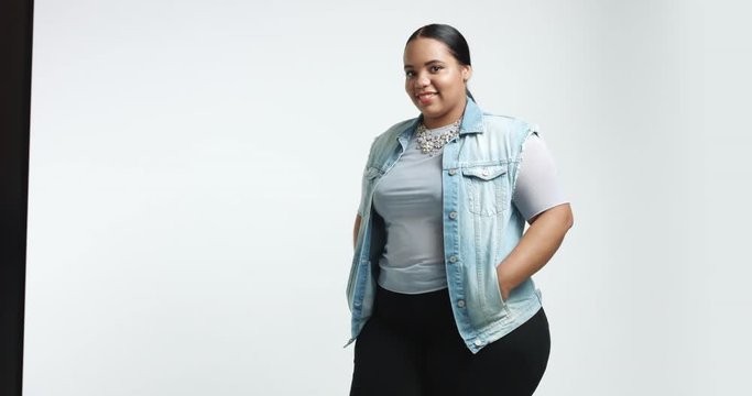Smiling cute big African American girl in blue shirt, black pants and a denim vest isolated on white. casual style plus size model