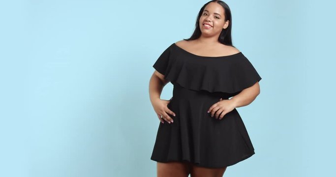 Dancing beautiful young plus size model in black short dress with ruffles isolated on colorful background