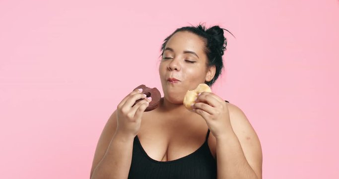 Attractive plus size model eating donuts and loving it on pink background