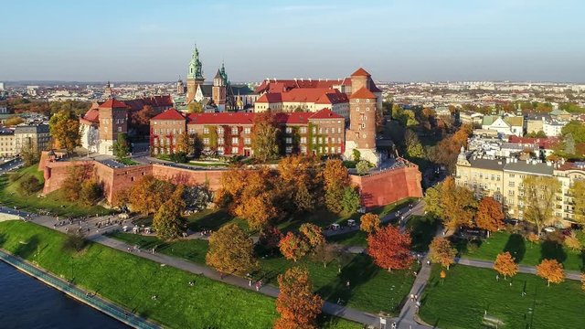 Krakow, Poland. Wawel royal Castle and Cathedral, Vistula River, park, promenade and walking people. Aerial 4K video in fall in sunset light