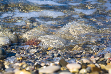 sea pebble beach with multicoloured stones, waves with foam