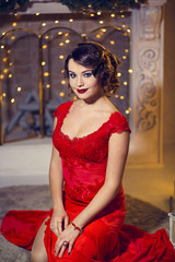 Brunette woman in red dress in luxury interior. Christmas tree. Presents and gift boxes under it. New Year decorations.