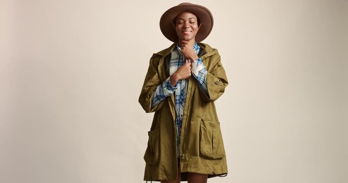 Pretty smiling mixed race female model wearing a plaid shirt over a short black skirt, khaki parka and a brown felt bush hat