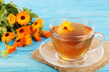 Calendula tea with fresh flowers on blue wooden background