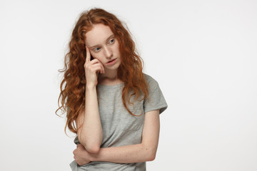Tired and bored redhead female in gray t-shirt, gesturing with hand, solving relationship or health problem. Doubt concept.