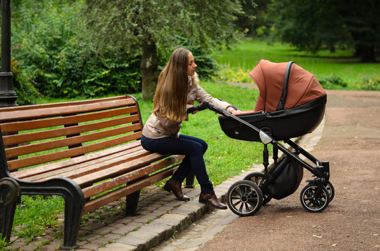 Family, child and motherhood concept - happy mother walking with baby stroller in park