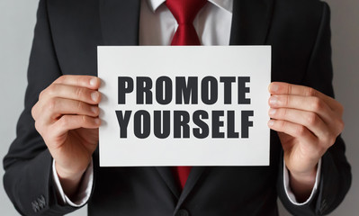 Obraz premium Businessman holding a card with text Promote Yourself