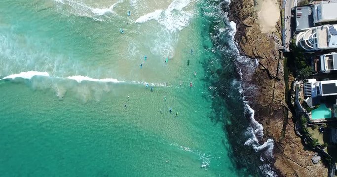 Waterfron at North side of Bondi beach and suburb with recreational surfers on surf boards riding the waves in top down aerial view.
